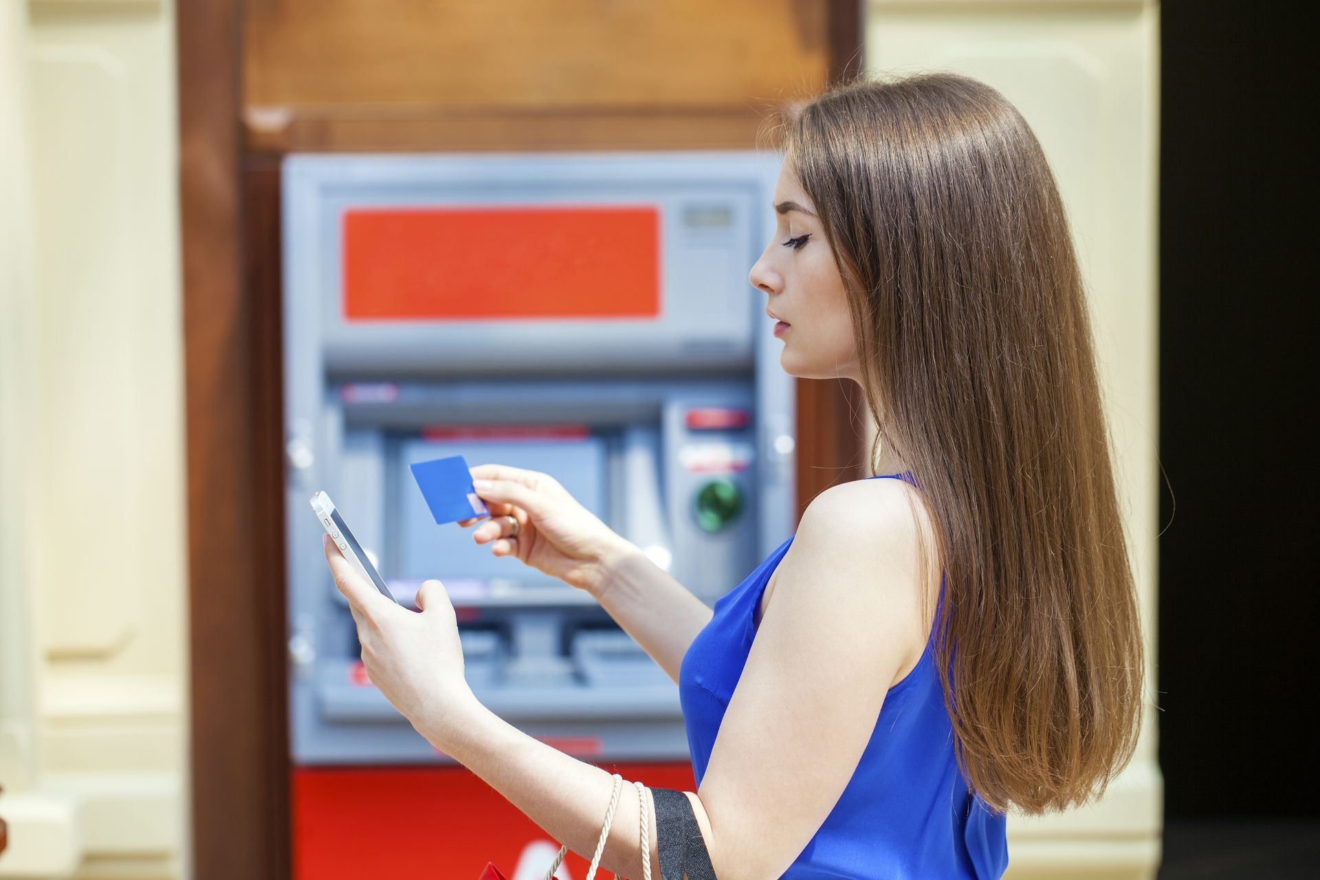 Young happy brunette woman withdrawing money from credit card at ATM, indoor shop